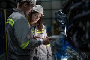 Factory engineer woman inspecting on machine with smart tablet. Worker works at machine robot arm. The welding machine with a remote system in an industrial factory. Artificial intelligence concept. photo