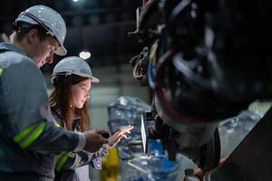 Factory engineer woman inspecting on machine with smart tablet. Worker works at machine robot arm. The welding machine with a remote system in an industrial factory. Artificial intelligence concept. photo