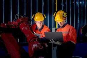 group of male engineer workers maintenance automatic robotic arm machine in a dark room factory. worker checking and repairing automatic robot hand machine. Worker wearing safety glasses and helmet. photo