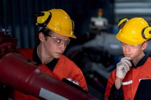 grupo de masculino ingeniero trabajadores mantenimiento automático robótico brazo máquina en un oscuro habitación fábrica. trabajador comprobación y reparando automático robot mano máquina. trabajador vistiendo la seguridad lentes y casco. foto