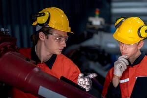 grupo de masculino ingeniero trabajadores mantenimiento automático robótico brazo máquina en un oscuro habitación fábrica. trabajador comprobación y reparando automático robot mano máquina. trabajador vistiendo la seguridad lentes y casco. foto