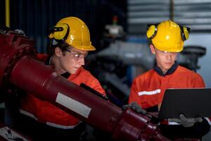 grupo de masculino ingeniero trabajadores mantenimiento automático robótico brazo máquina en un oscuro habitación fábrica. trabajador comprobación y reparando automático robot mano máquina. trabajador vistiendo la seguridad lentes y casco. foto