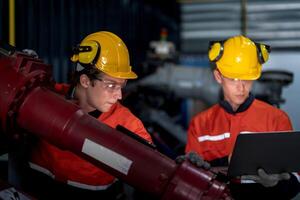 group of male engineer workers maintenance automatic robotic arm machine in a dark room factory. worker checking and repairing automatic robot hand machine. Worker wearing safety glasses and helmet. photo