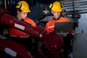 group of male engineer workers maintenance automatic robotic arm machine in a dark room factory. worker checking and repairing automatic robot hand machine. Worker wearing safety glasses and helmet. photo