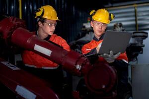 group of male engineer workers maintenance automatic robotic arm machine in a dark room factory. worker checking and repairing automatic robot hand machine. Worker wearing safety glasses and helmet. photo