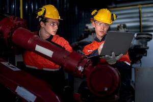 group of male engineer workers maintenance automatic robotic arm machine in a dark room factory. worker checking and repairing automatic robot hand machine. Worker wearing safety glasses and helmet. photo