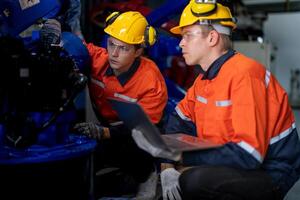 Factory engineers inspecting on machine with smart tablet. Worker works at heavy machine robot arm. The welding machine with a remote system in an industrial factory. Artificial intelligence concept. photo