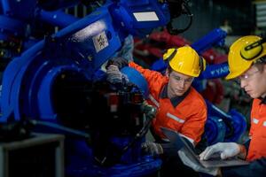 Factory engineers inspecting on machine with smart tablet. Worker works at heavy machine robot arm. The welding machine with a remote system in an industrial factory. Artificial intelligence concept. photo