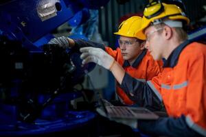 negocio ingenieros reunirse y cheque controlar pesado máquina robot brazo. diverso equipo de industrial robótica ingenieros reunido alrededor máquina. profesional maquinaria operador utilizar industrial digital tableta. foto