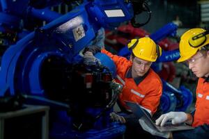 fábrica ingenieros inspeccionando en máquina con inteligente tableta. trabajador trabajos a pesado máquina robot brazo. el soldadura máquina con un remoto sistema en un industrial fábrica. artificial inteligencia concepto. foto