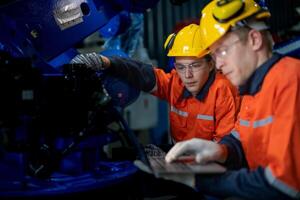 negocio ingenieros reunirse y cheque controlar pesado máquina robot brazo. diverso equipo de industrial robótica ingenieros reunido alrededor máquina. profesional maquinaria operador utilizar industrial digital tableta. foto