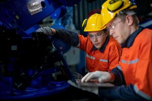 fábrica ingenieros inspeccionando en máquina con inteligente tableta. trabajador trabajos a pesado máquina robot brazo. el soldadura máquina con un remoto sistema en un industrial fábrica. artificial inteligencia concepto. foto