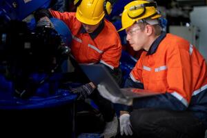 negocio ingenieros reunirse y cheque controlar pesado máquina robot brazo. diverso equipo de industrial robótica ingenieros reunido alrededor máquina. profesional maquinaria operador utilizar industrial digital tableta. foto