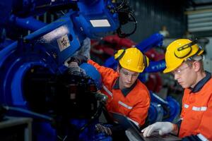 Factory engineers inspecting on machine with smart tablet. Worker works at heavy machine robot arm. The welding machine with a remote system in an industrial factory. Artificial intelligence concept. photo