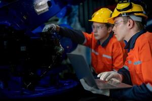 Factory engineers inspecting on machine with smart tablet. Worker works at heavy machine robot arm. The welding machine with a remote system in an industrial factory. Artificial intelligence concept. photo