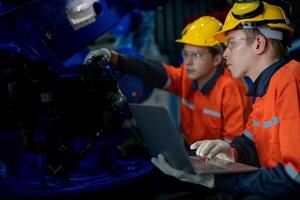 Factory engineers inspecting on machine with smart tablet. Worker works at heavy machine robot arm. The welding machine with a remote system in an industrial factory. Artificial intelligence concept. photo