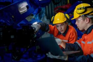 Factory engineers inspecting on machine with smart tablet. Worker works at heavy machine robot arm. The welding machine with a remote system in an industrial factory. Artificial intelligence concept. photo