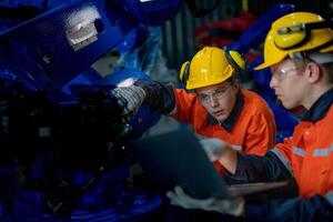 Factory engineers inspecting on machine with smart tablet. Worker works at heavy machine robot arm. The welding machine with a remote system in an industrial factory. Artificial intelligence concept. photo