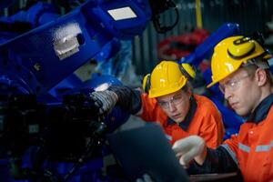 negocio ingenieros reunirse y cheque controlar pesado máquina robot brazo. diverso equipo de industrial robótica ingenieros reunido alrededor máquina. profesional maquinaria operador utilizar industrial digital tableta. foto