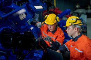 Factory engineers inspecting on machine with smart tablet. Worker works at heavy machine robot arm. The welding machine with a remote system in an industrial factory. Artificial intelligence concept. photo