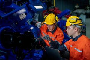 Factory engineers inspecting on machine with smart tablet. Worker works at heavy machine robot arm. The welding machine with a remote system in an industrial factory. Artificial intelligence concept. photo