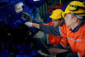 Factory engineers inspecting on machine with smart tablet. Worker works at heavy machine robot arm. The welding machine with a remote system in an industrial factory. Artificial intelligence concept. photo