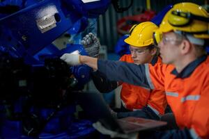 Factory engineers inspecting on machine with smart tablet. Worker works at heavy machine robot arm. The welding machine with a remote system in an industrial factory. Artificial intelligence concept. photo