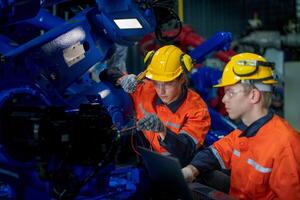 Factory engineers inspecting on machine with smart tablet. Worker works at heavy machine robot arm. The welding machine with a remote system in an industrial factory. Artificial intelligence concept. photo