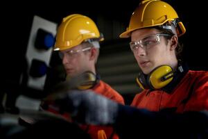 Engineer man checking the status of machine and used wrench to screw some part of equipment at CNC factory. Worker wearing safety glasses and helmet. Maintenance and repairing concept. photo