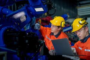 Factory engineers inspecting on machine with smart tablet. Worker works at heavy machine robot arm. The welding machine with a remote system in an industrial factory. Artificial intelligence concept. photo