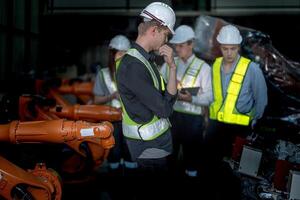 Sales manager and factory owner in suits negotiating selling robots used in the factory. Business engineers meeting and checking new machine robot. Workers walking at warehouse welding machine. photo