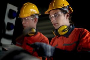 Engineer man checking the status of machine and used wrench to screw some part of equipment at CNC factory. Worker wearing safety glasses and helmet. Maintenance and repairing concept. photo