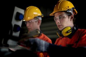 Engineer man checking the status of machine and used wrench to screw some part of equipment at CNC factory. Worker wearing safety glasses and helmet. Maintenance and repairing concept. photo