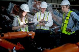 Business engineers meeting and checking new machine robot. Workers walking at warehouse industry welding machine. business negotiation concepts and technology. women Using smart Tablet to present man. photo