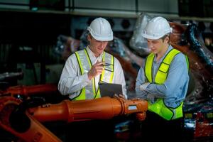 Business engineers meeting and checking new machine robot. Workers walking at warehouse industry welding machine. business negotiation concepts and technology. women Using smart Tablet to present man. photo