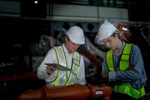 Sales manager and factory owner in suits negotiating selling robots used in the factory. Business engineers meeting and checking new machine robot. Workers walking at warehouse welding machine. photo