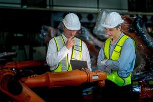 Business engineers meeting and checking new machine robot. Workers walking at warehouse industry welding machine. business negotiation concepts and technology. women Using smart Tablet to present man. photo