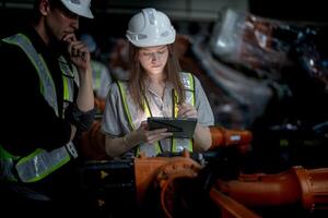 Business engineers meeting and checking new machine robot. Workers walking at warehouse industry welding machine. business negotiation concepts and technology. women Using smart Tablet to present man. photo