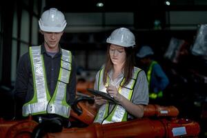 Business engineers meeting and checking new machine robot. Workers walking at warehouse industry welding machine. business negotiation concepts and technology. women Using smart Tablet to present man. photo