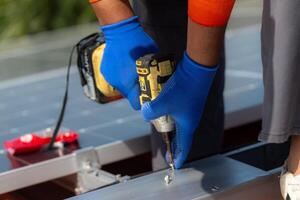 cerca arriba mano utilizando perforar conductor equipo en estructura. ingeniero hombre es trabajando a construir solar paneles sistema en techo. instalando solar fotovoltaica panel sistema. foto