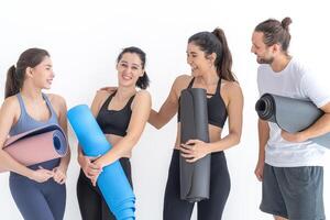Group of happy sporty women talking with body stylish sportswear holding personal carpets leaned on a white background. waiting for yoga class or body weight class. healthy lifestyle and wellness photo