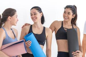 grupo de contento deportivo mujer hablando con cuerpo elegante ropa de deporte participación personal alfombras inclinado en un blanco antecedentes. esperando para yoga clase o cuerpo peso clase. sano estilo de vida y bienestar foto