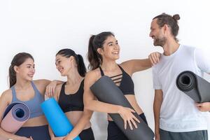 Group of happy sporty women and guy wearing body stylish sportswear holding personal carpets leaned on a white background. waiting for yoga class or body weight class. healthy lifestyle and wellness photo