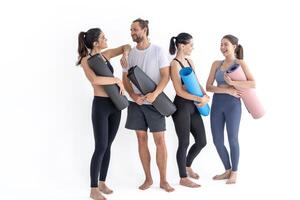 grupo de contento deportivo muchachas y chico vistiendo cuerpo elegante ropa de deporte participación personal alfombras inclinado en un blanco antecedentes. esperando para yoga clase o cuerpo peso clase. sano estilo de vida y bienestar foto