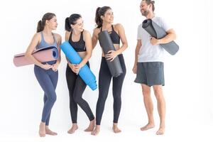 Group of happy sporty women and guy wearing body stylish sportswear holding personal carpets leaned on a white background. waiting for yoga class or body weight class. healthy lifestyle and wellness photo