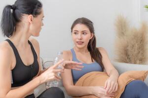 Group of happy sporty women wearing body stylish sportswear and talking together. waiting for yoga class.. healthy lifestyle and wellness. Couple women are relaxing and sitting at sofa in living room. photo