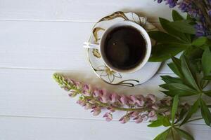 A cup of coffee and lupine flowers on a white wooden table. photo