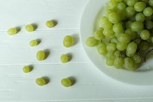 Ripe grapes in a plate on a white wooden table. Top view. photo