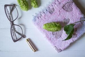 The closed pink notepad, pen, white candle and branches of hops as decoration on a white wooden table. Desktop still life. photo