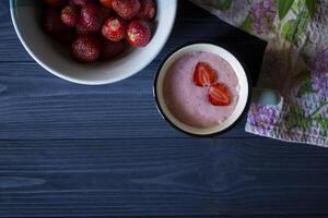 Strawberry dessert. A mug with strawberry creamy fresh, bowl with ripe strawberries and lupine on a dark blue wooden table. Beautiful food still life. photo